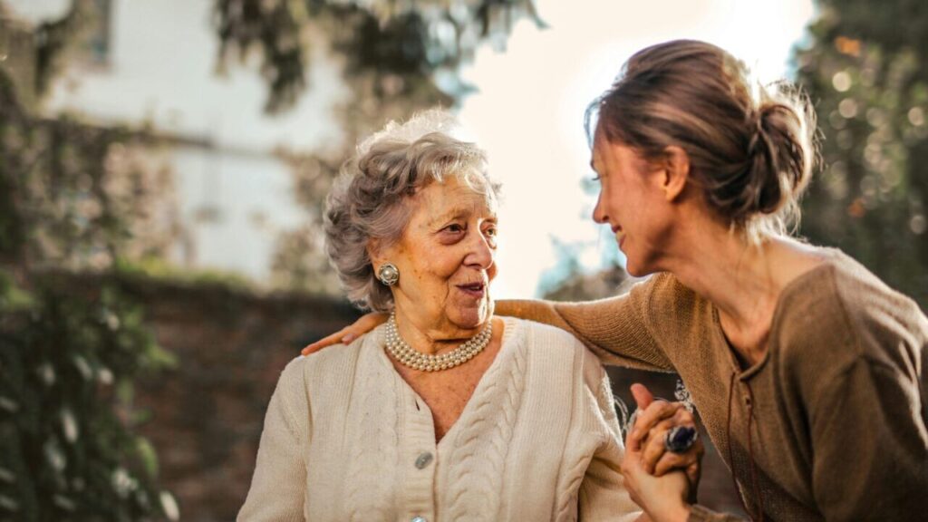 Home Elderly woman and adult daughter share a joyful, affectionate moment in a sunny garden.
